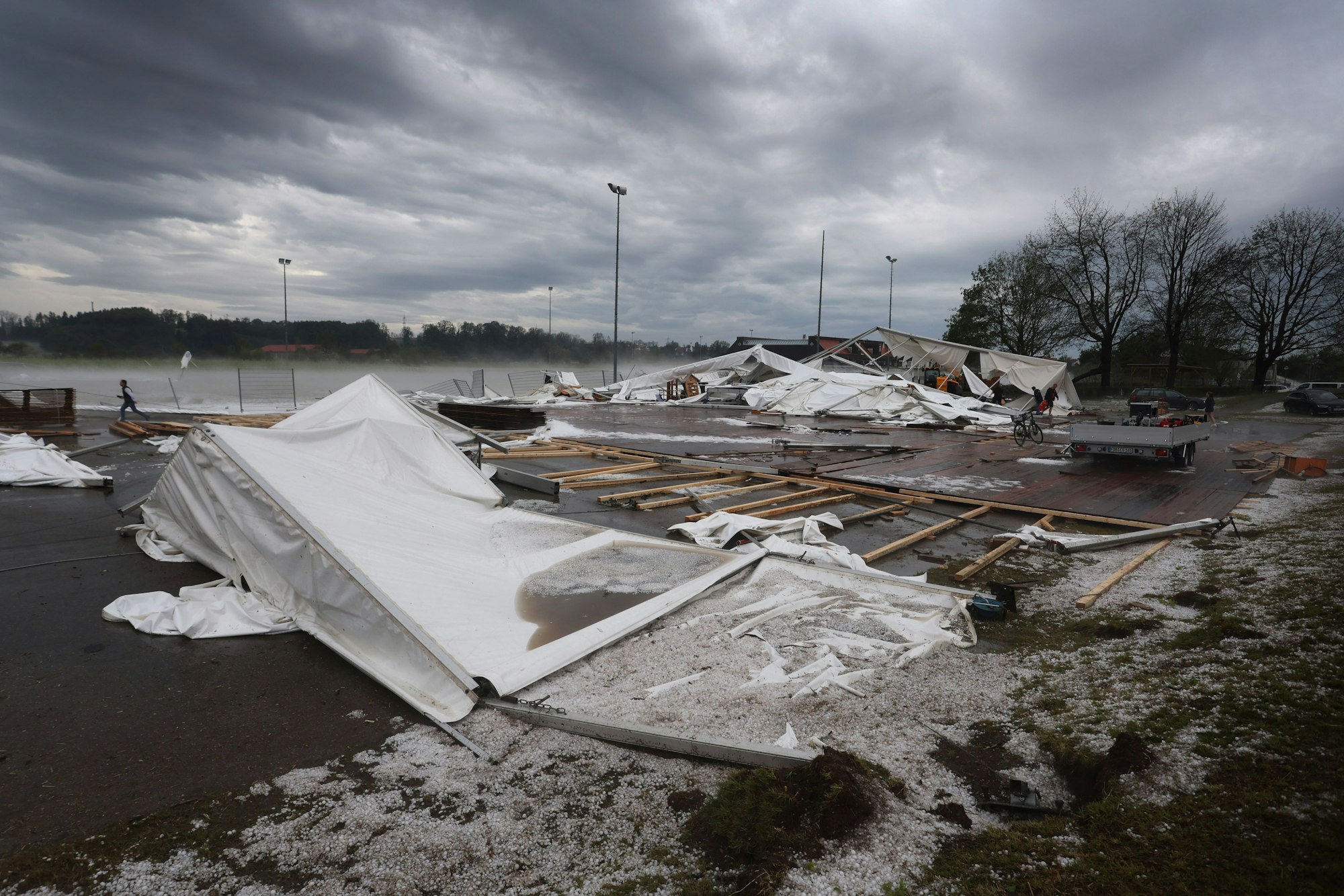 Reste eines vom Sturm zerstörten Festzeltes liegen am Ortsrand von Kissing. Auf der Wiese davor ist Hagel zu sehen.