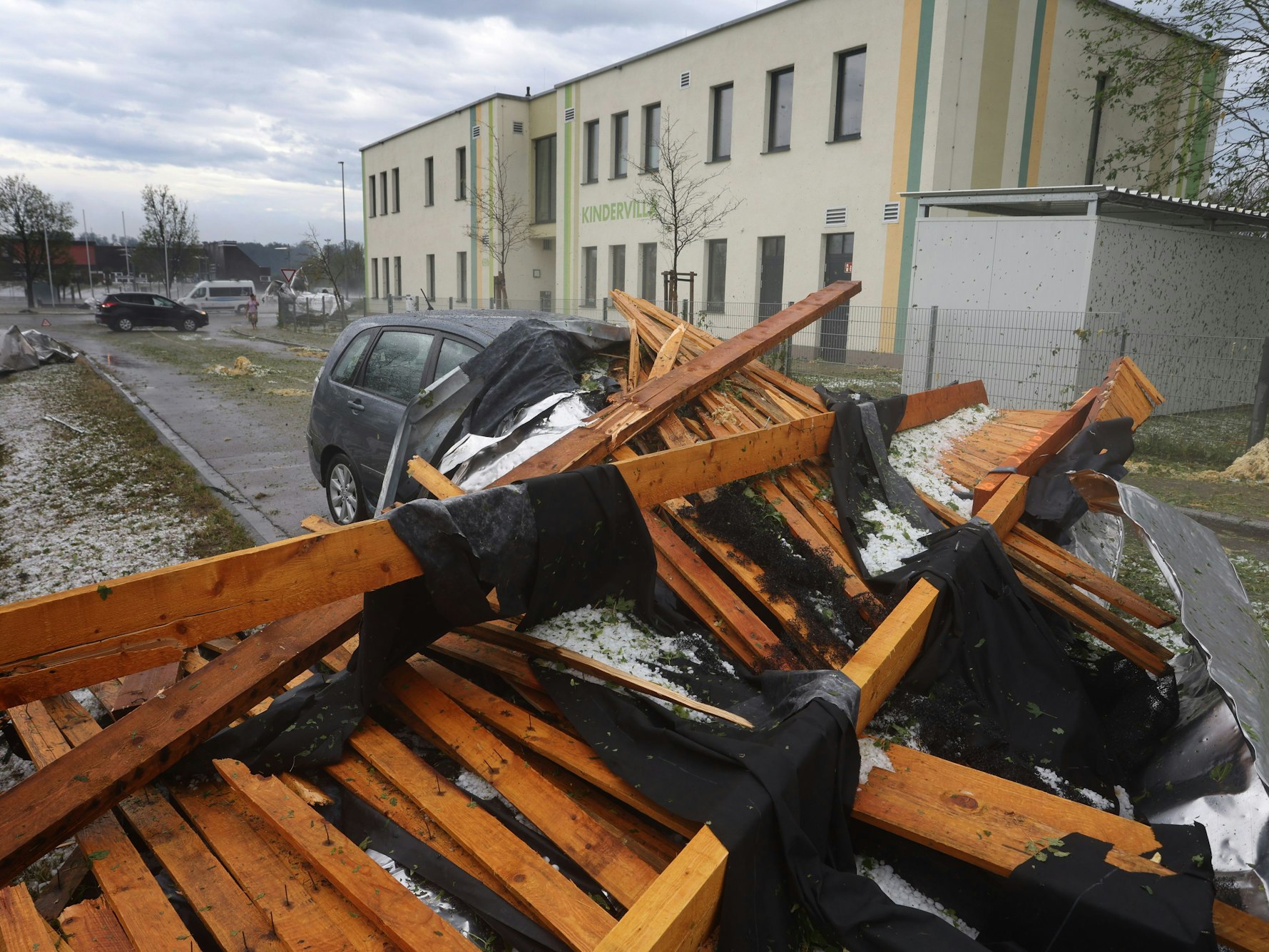 Ein vom Sturm abgetragenes Dach eines Seniorenheims liegt auf einem Parkplatz auf einem Auto.