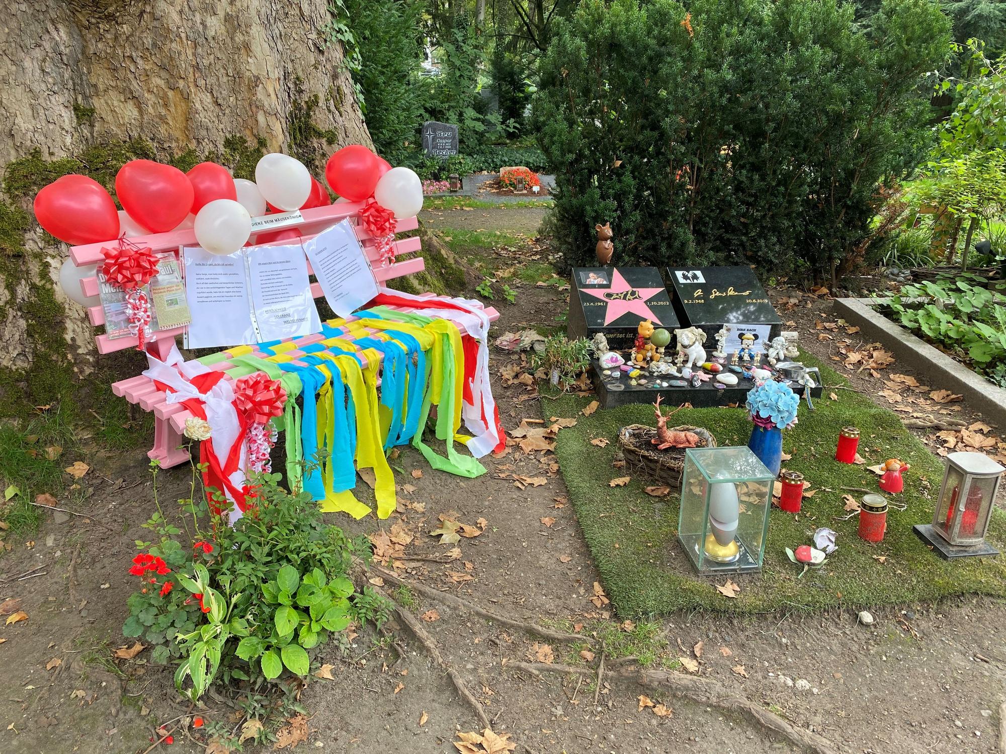 Blick auf das Grab von Dirk Bach auf dem Melatenfriedhof in Köln. Die rosa Bank, die als gestohlen gemeldet wurde, ist wieder da und sieht festlich geschmückt aus.