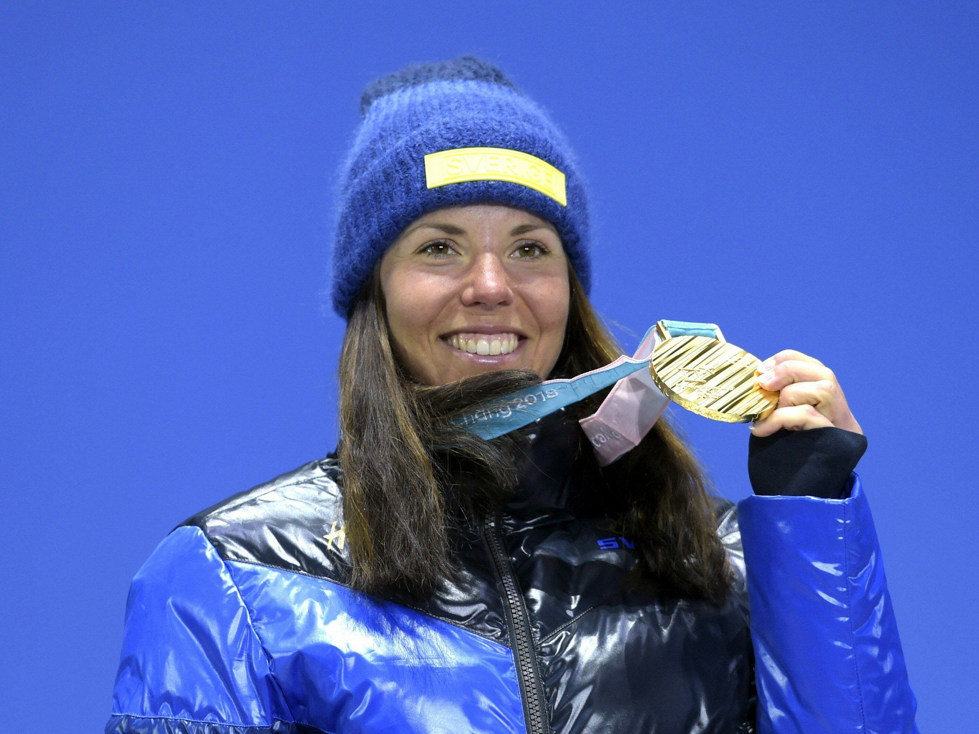 Skiathlon-Olympiasiegerin Charlotte Kalla aus Schweden steht während der Siegerehrung auf dem Podium und zeigt ihre Medaille.