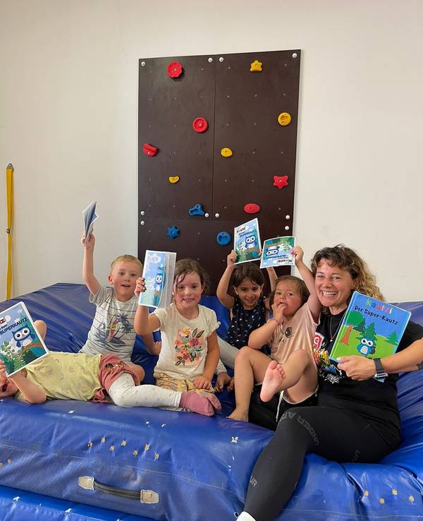 Eine Frau sitzt mit Kindern auf einer Sportmatte und hält Buch in der Hand.