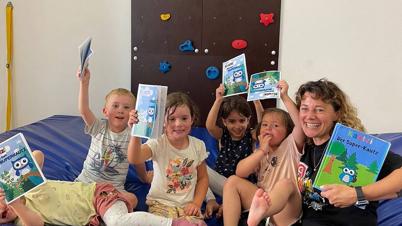 Eine Frau sitzt mit Kindern auf einer Sportmatte und hält Buch in der Hand.