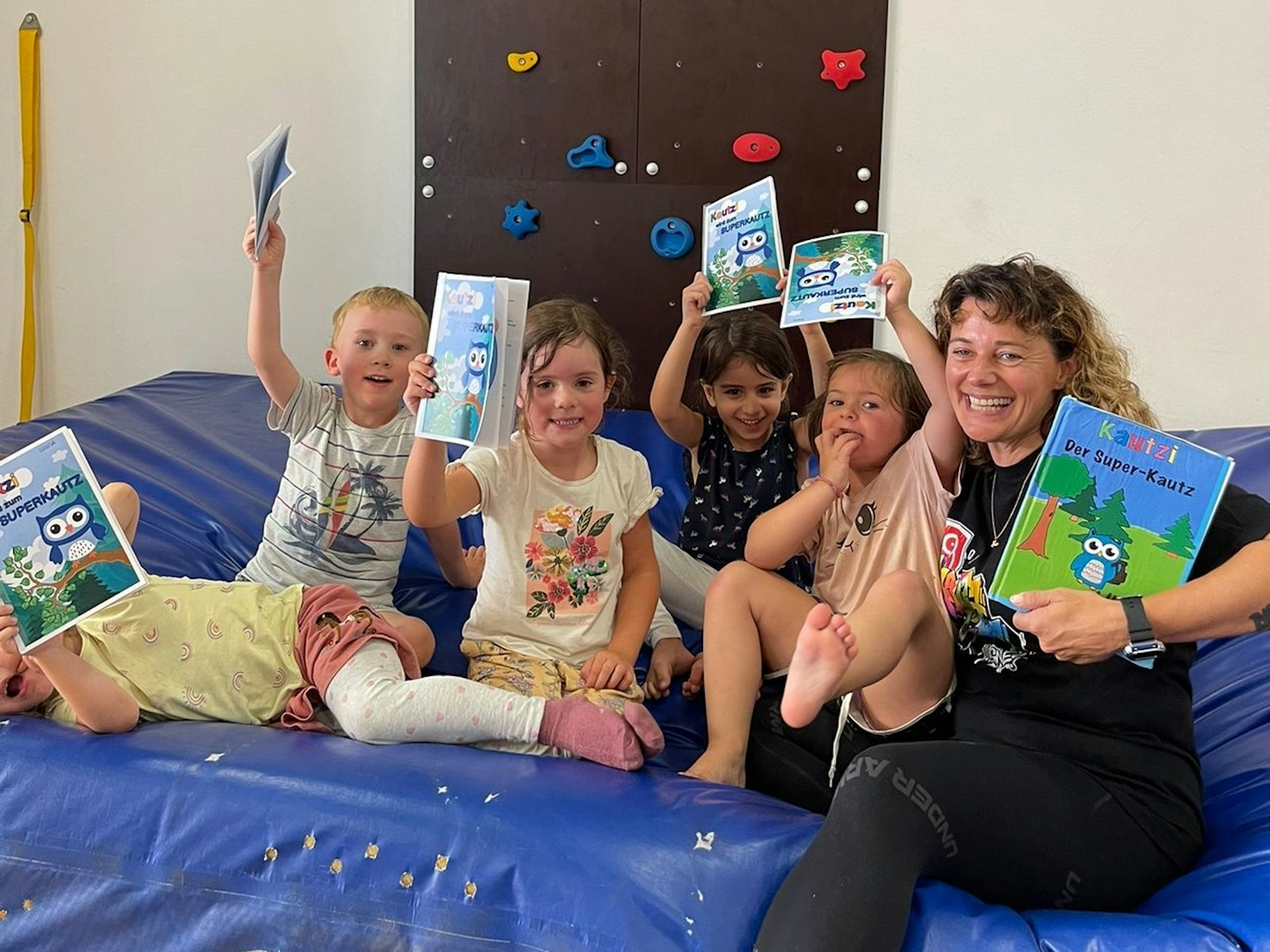 Eine Frau sitzt mit Kindern auf einer Sportmatte und hält Buch in der Hand.