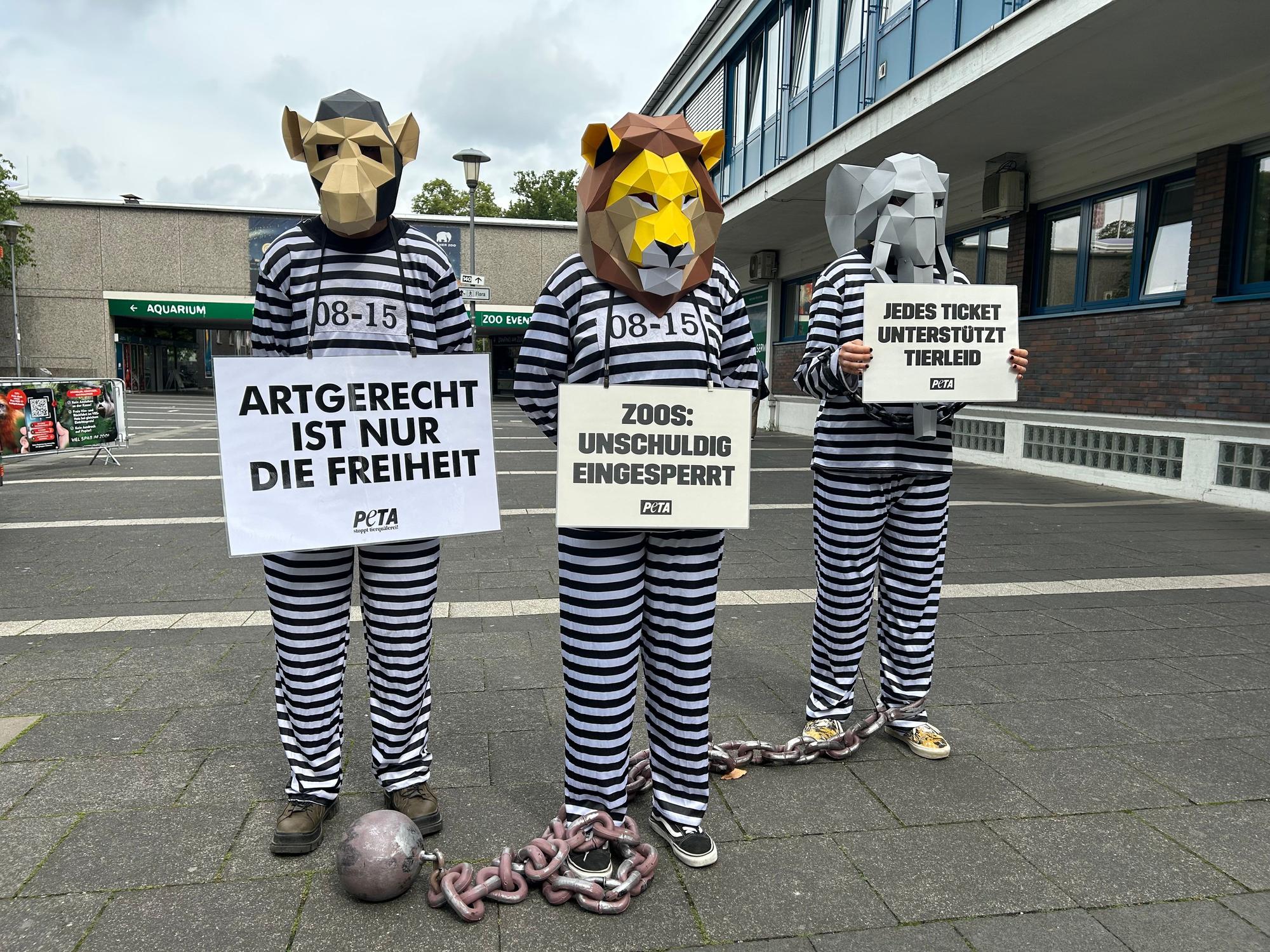 Drei wie Häftlinge verkleidete Aktivistinnen und Aktivisten, mit Demo-Bannern und Tierkopf-Masken.