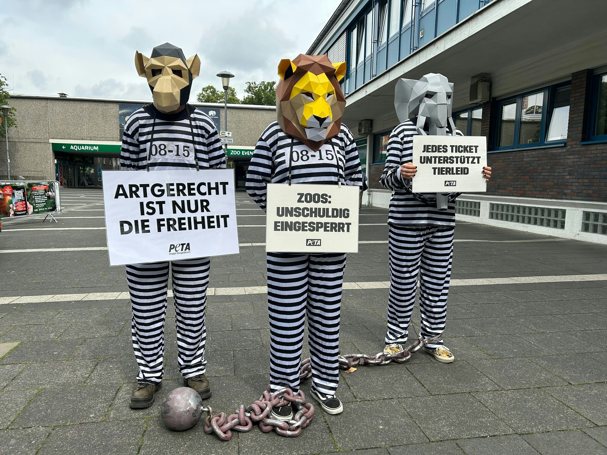 Drei wie Häftlinge verkleidete Aktivistinnen und Aktivisten, mit Demo-Bannern und Tierkopf-Masken.