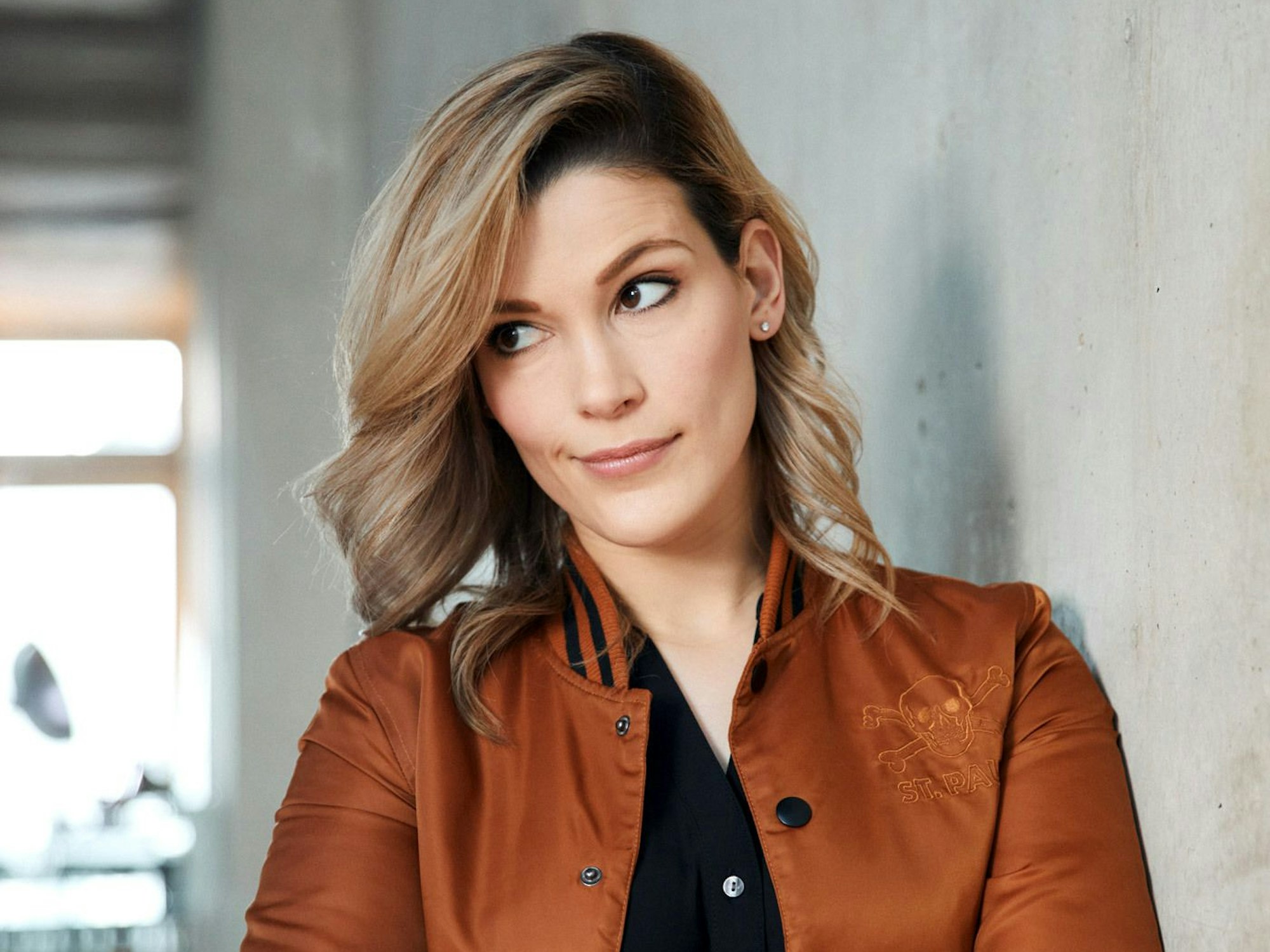 Melek Balgün lehnt an einer Wand und schaut nach rechts.