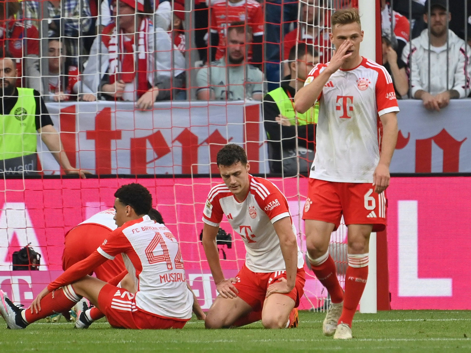 Jamal Musiala sitzt, Benjamin Pavard kniet, Joshua Kimmich steht.