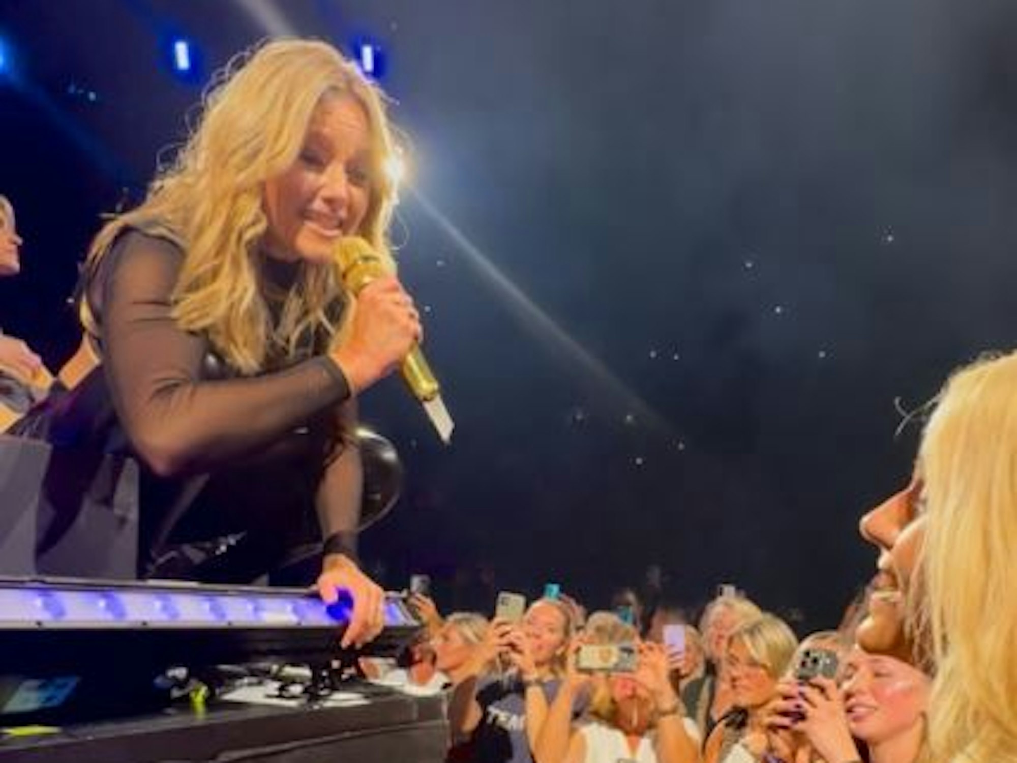 Helene Fischer kniet auf der Bühne und hält einer anderen Frau das Mikrofon hin.