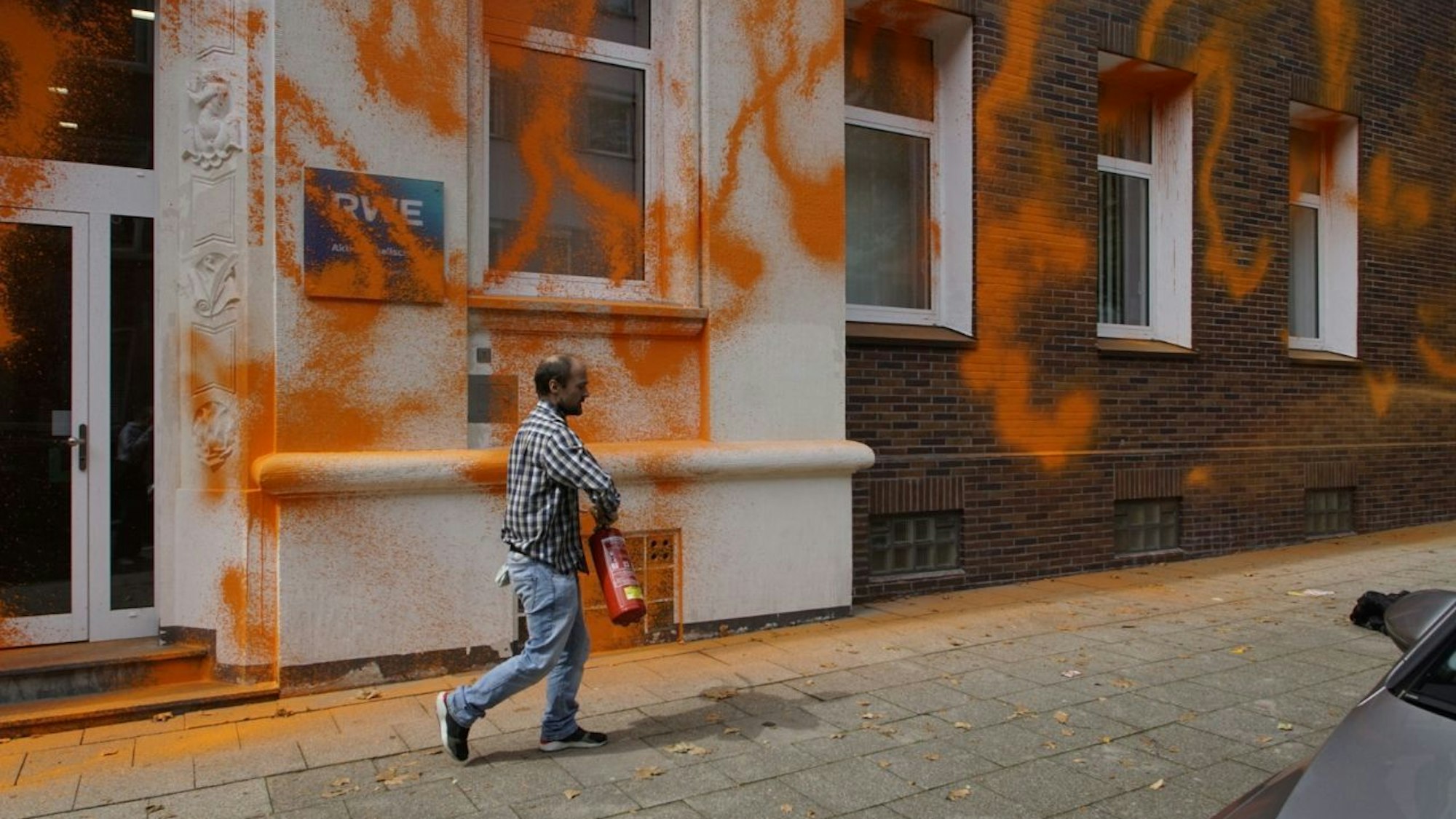Mann besprüht eine Hauswand mit orangener Farbe.
