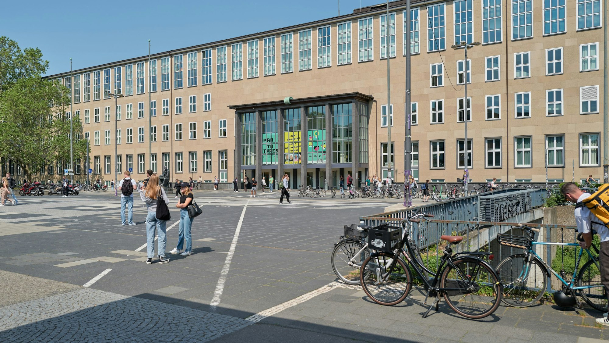 Der Haupteingang der Universität zu Köln mit diversen Studierenden davor.