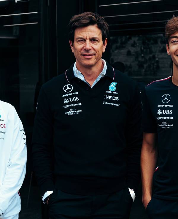 Lewis Hamilton (li.), Toto Wolff (Mitte) und George Russell (re.) posieren für ein Foto und lächeln.