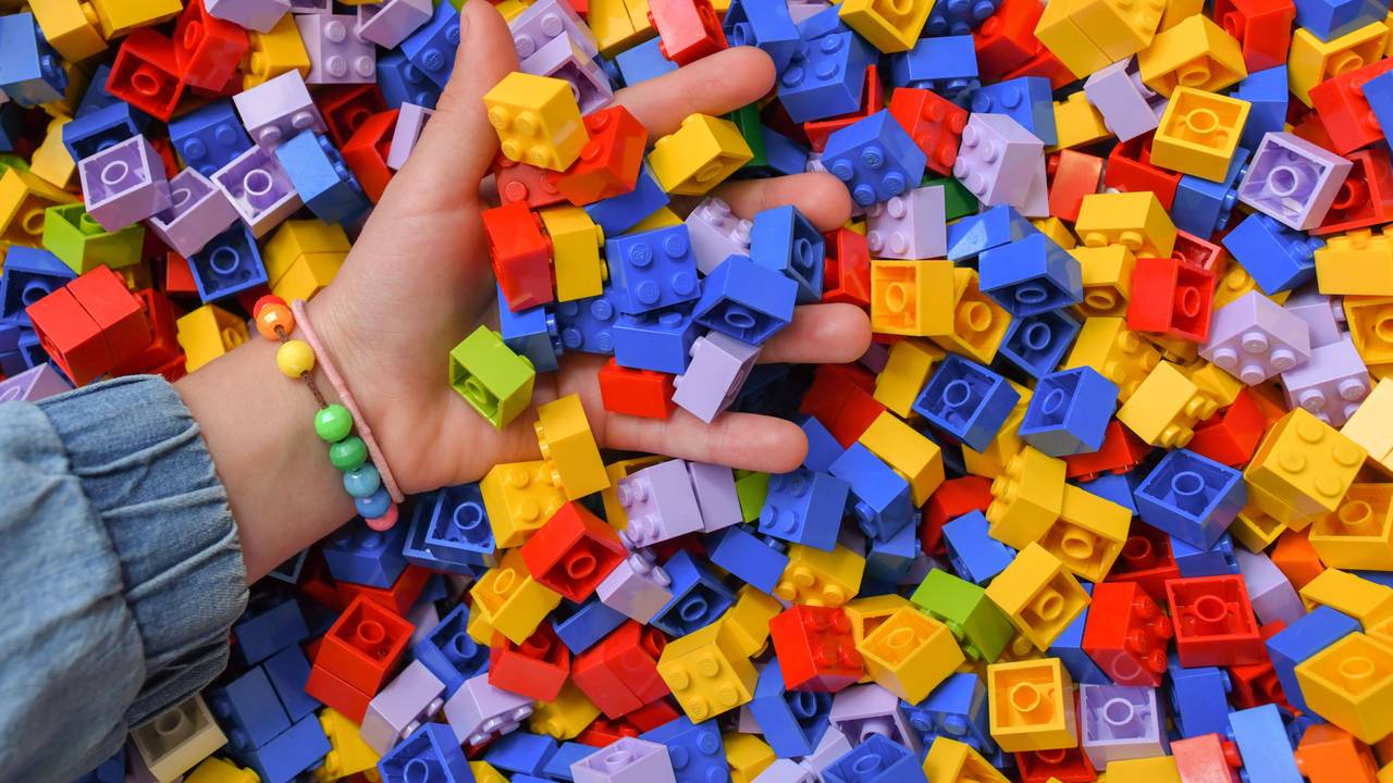 Ein Mädchen greift in eine Kiste voller Lego-Steine.
