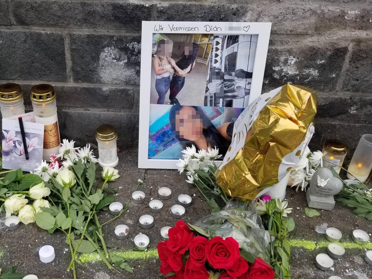 Vor einer Mauer stehen Fotos und Kerzen, liegen Blumen.