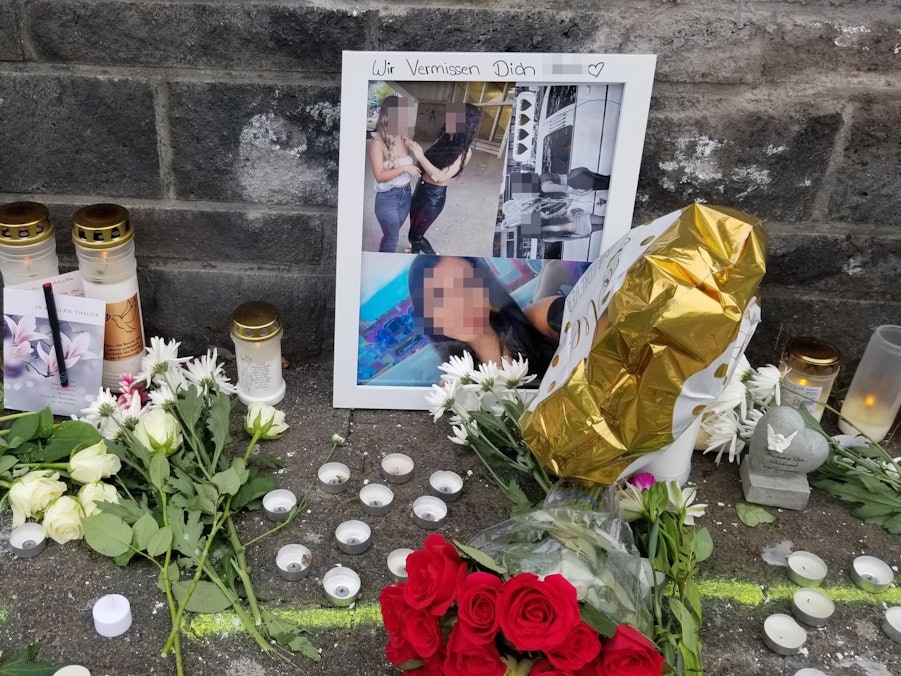 Vor einer Mauer stehen Fotos und Kerzen, liegen Blumen.