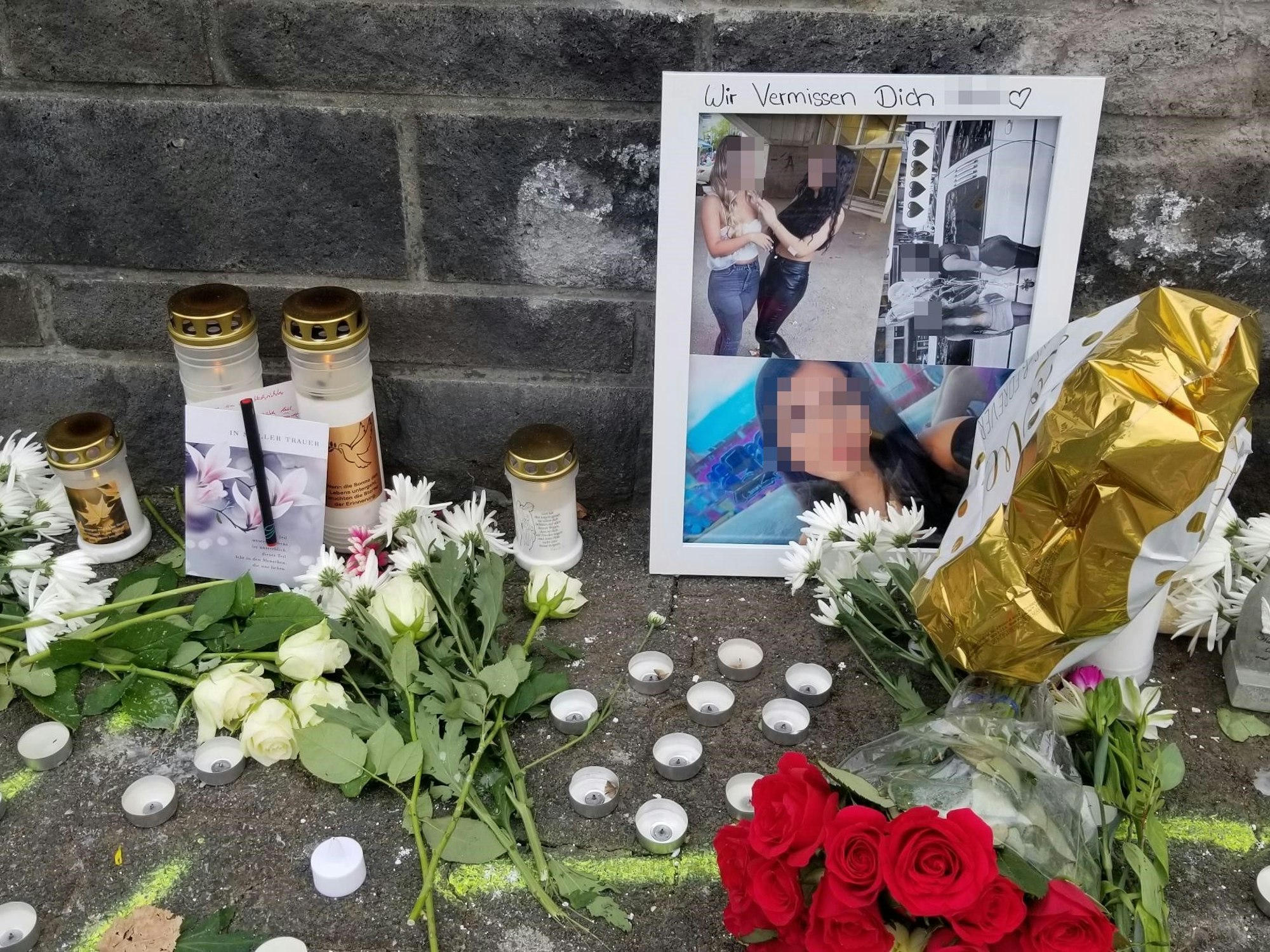 Blumen liegen an einer Mauer, Kerzen und Fotos wurden aufgestellt.