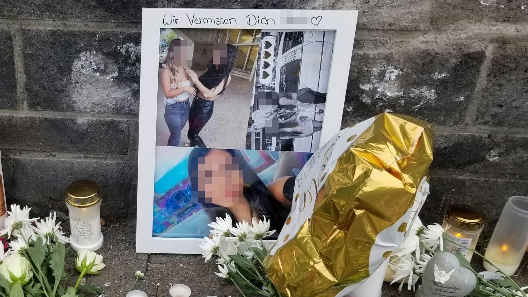 Fotos von Matilda sind an eine Mauer gelehnt, davor stehen Kerzen und liegen Blumen.