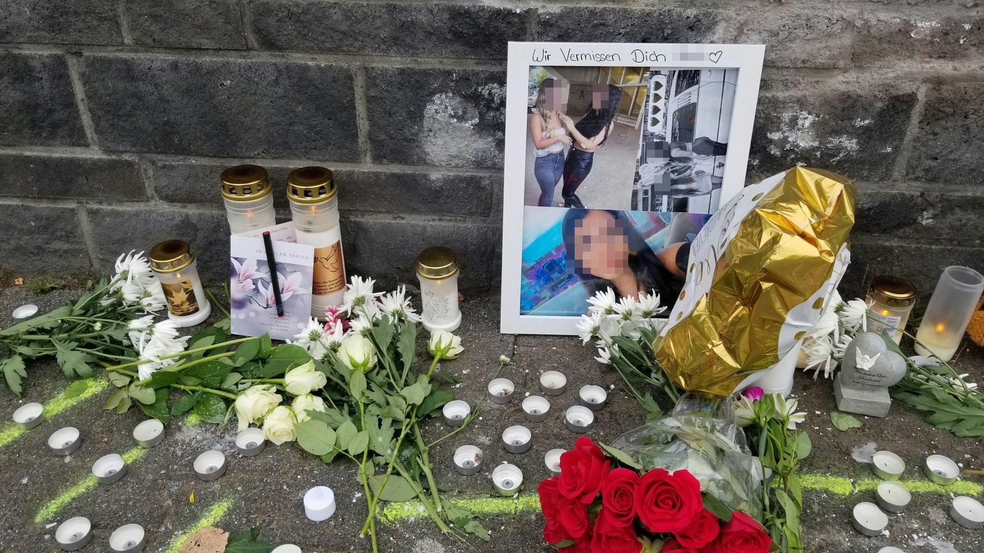 Vor einer Mauer stehen Fotos und Kerzen, liegen Blumen.