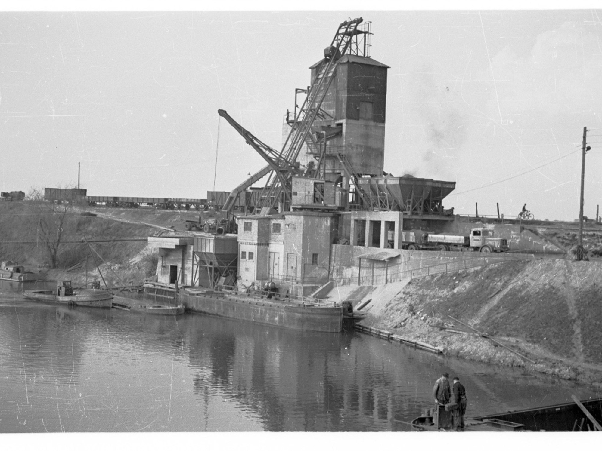Kiesabbau in der Kiesbaggerei zwischen Esch und Pesch. Hier befindet sich heute der Escher See in Köln. Was das Foto aufgenommen wurde, ist nicht bekannt. Auf dem Bild ist vermutlich die Schute zu sehen, die jetzt als Wrack im Escher See liegt.