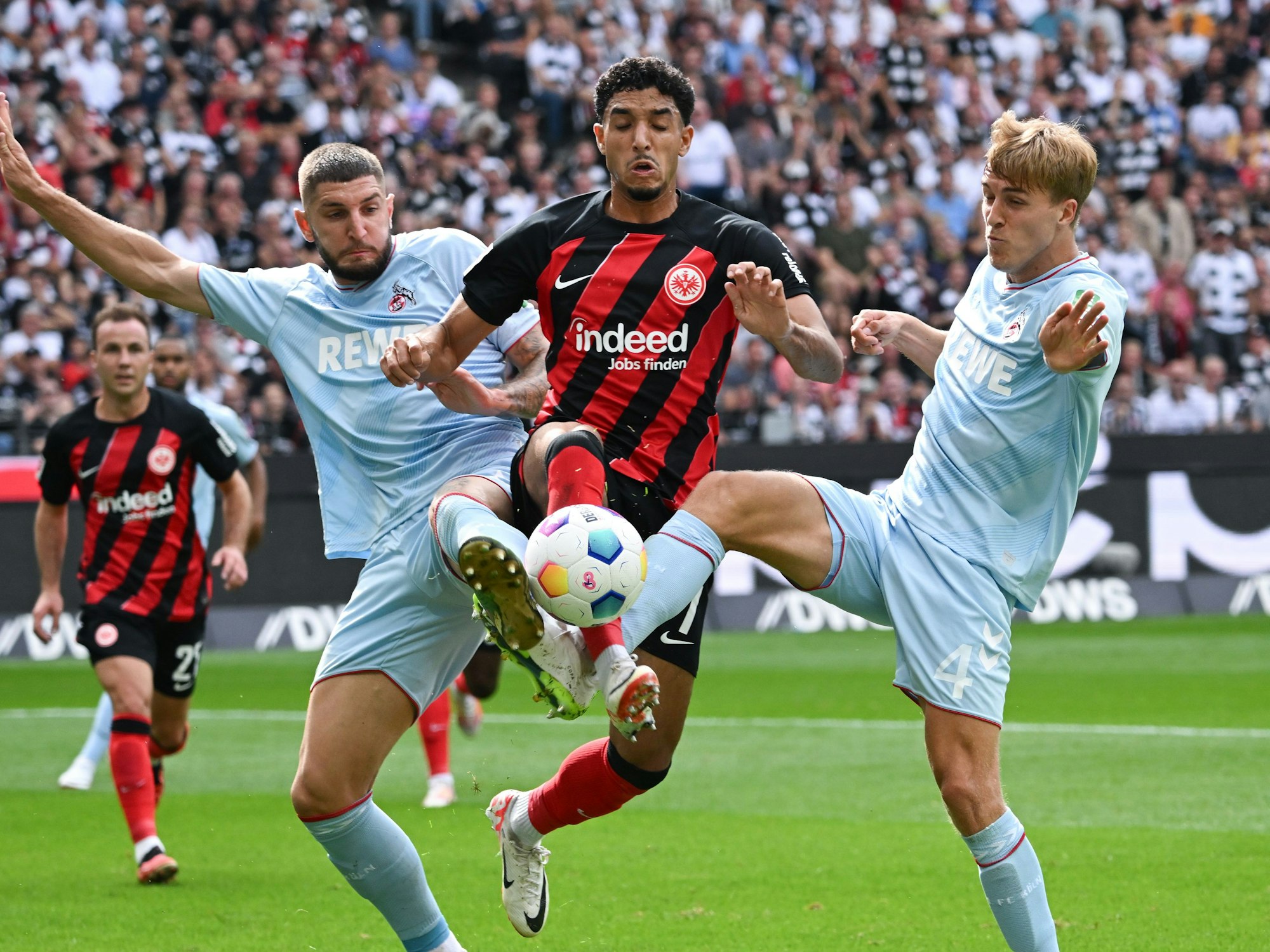Frankfurts Omar Marmoush (M) und die Kölner Jeff Chabot (l) und Timo Hübers kämpfen um den Ball.