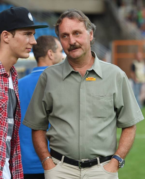 Peter Neururer hat die Hände in den Hosentaschen. Neben ihm steht Leon Goretzka. Er trägt eine Kappe.