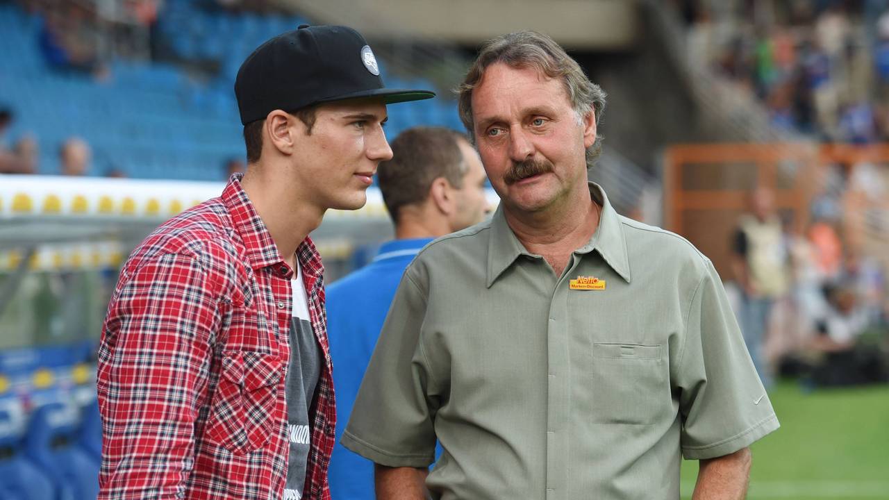 Peter Neururer hat die Hände in den Hosentaschen. Neben ihm steht Leon Goretzka. Er trägt eine Kappe.