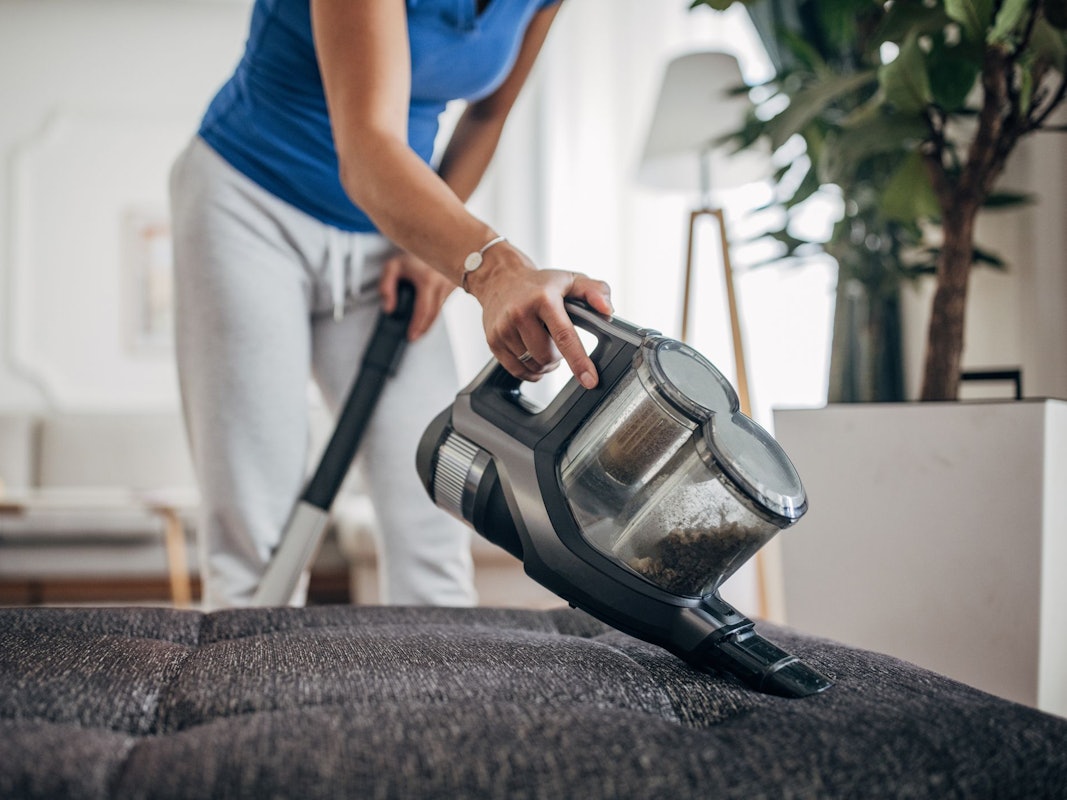 Eine Frau saugt mit einem Akkustaubsauger ihr Sofa ab.