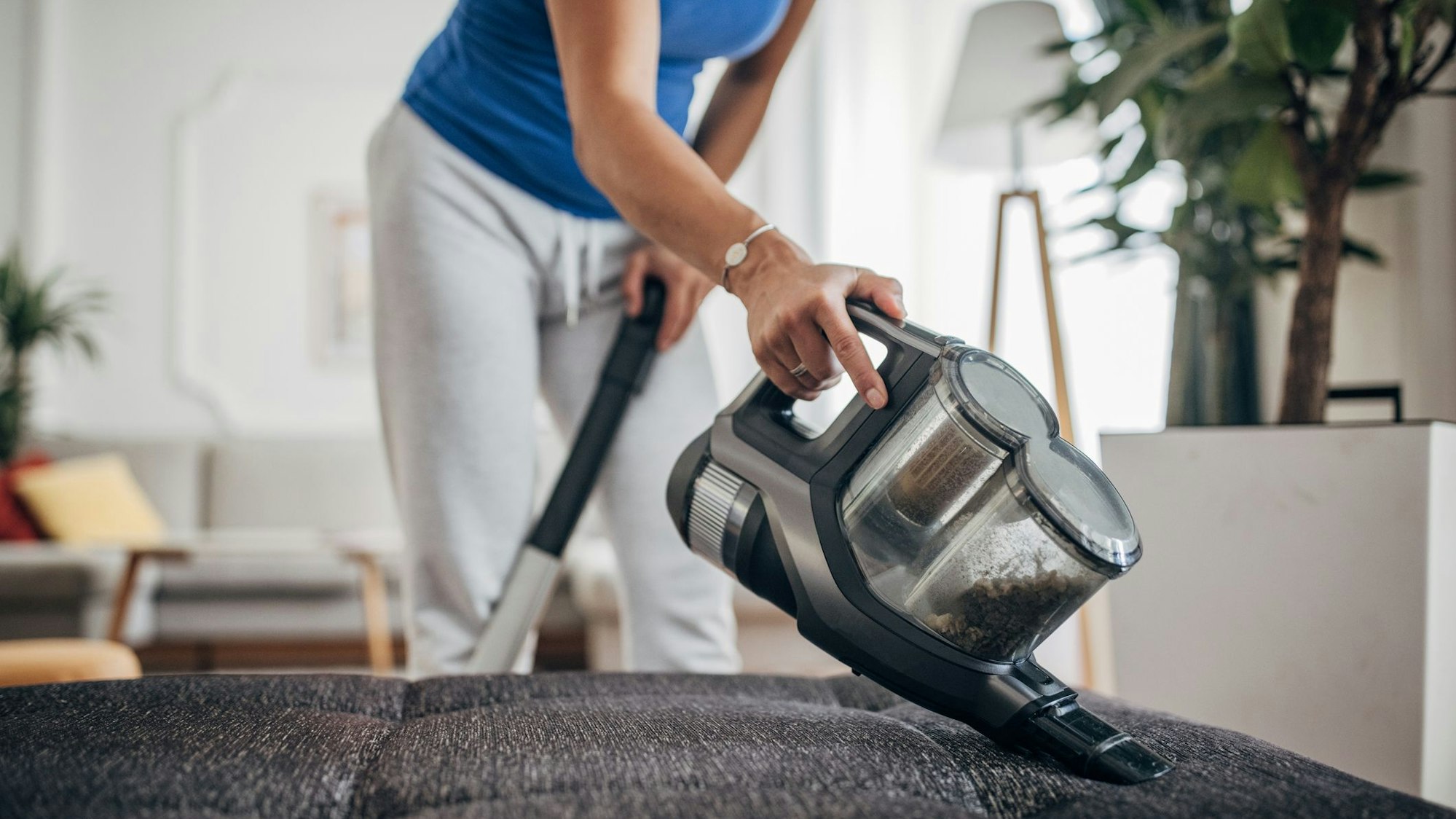 Eine Frau saugt mit einem Akkustaubsauger ihr Sofa ab.