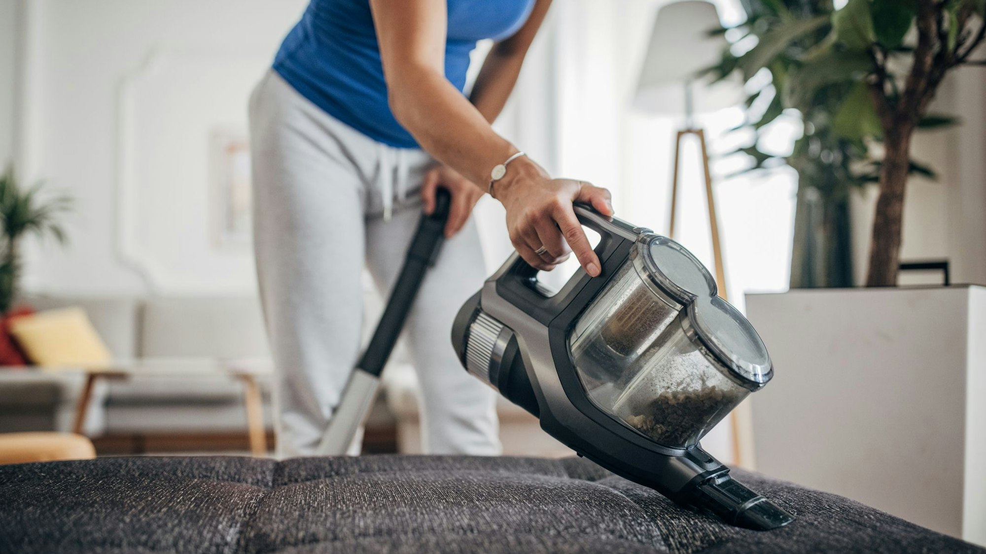 Eine Frau saugt mit einem Akkustaubsauger ihr Sofa ab.