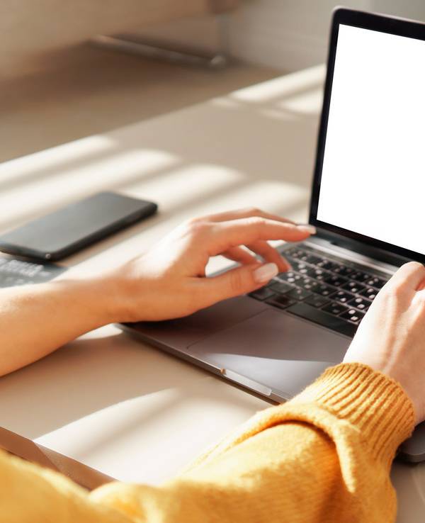 Eine Frau tippt auf einem Notebook. Neben ihr steht ein Glas mit Tee.
