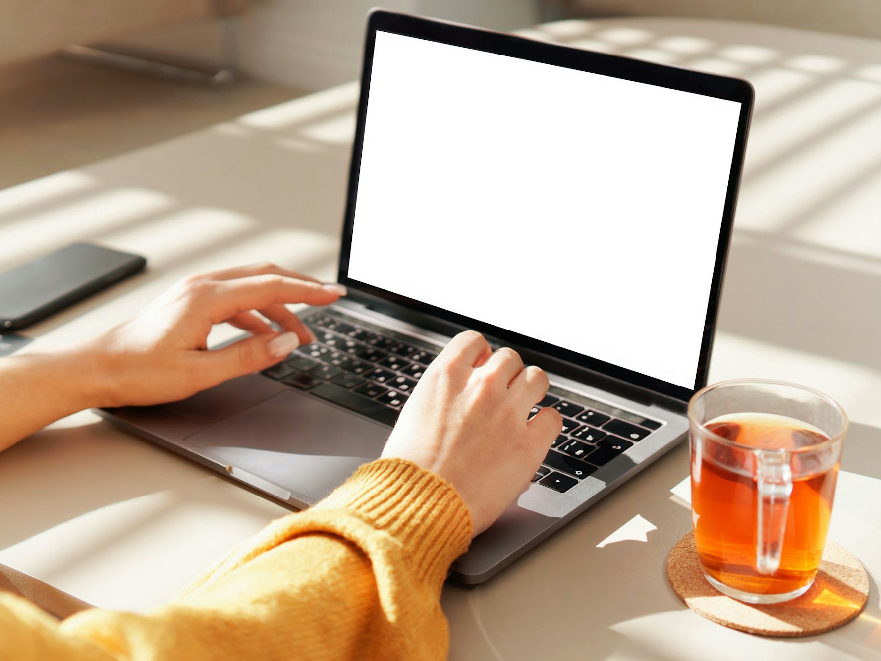Eine Frau tippt auf einem Notebook. Neben ihr steht ein Glas mit Tee.