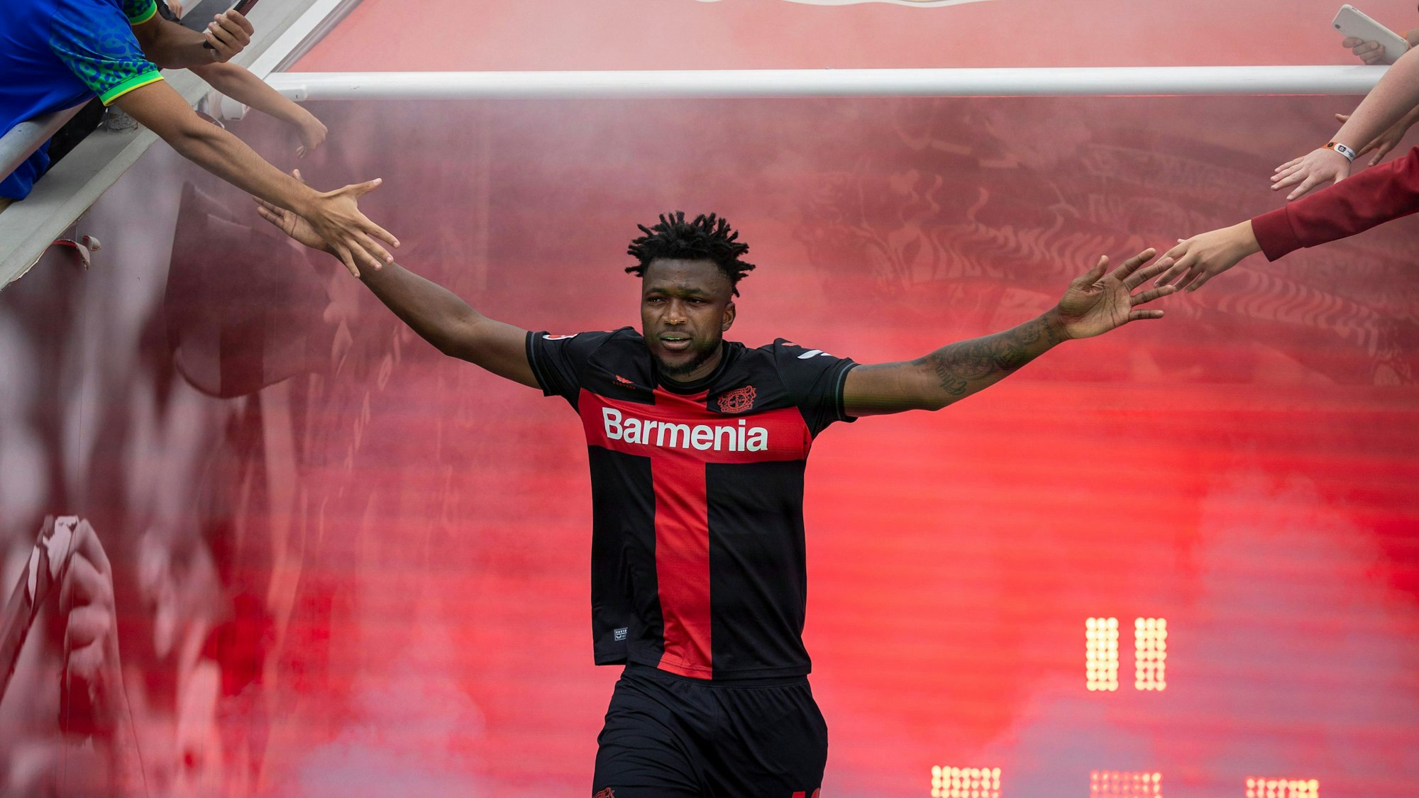 Edmond Taposoba kommt in Stadion, breitet seine Arme aus. Fans reichen ihm die Hände.