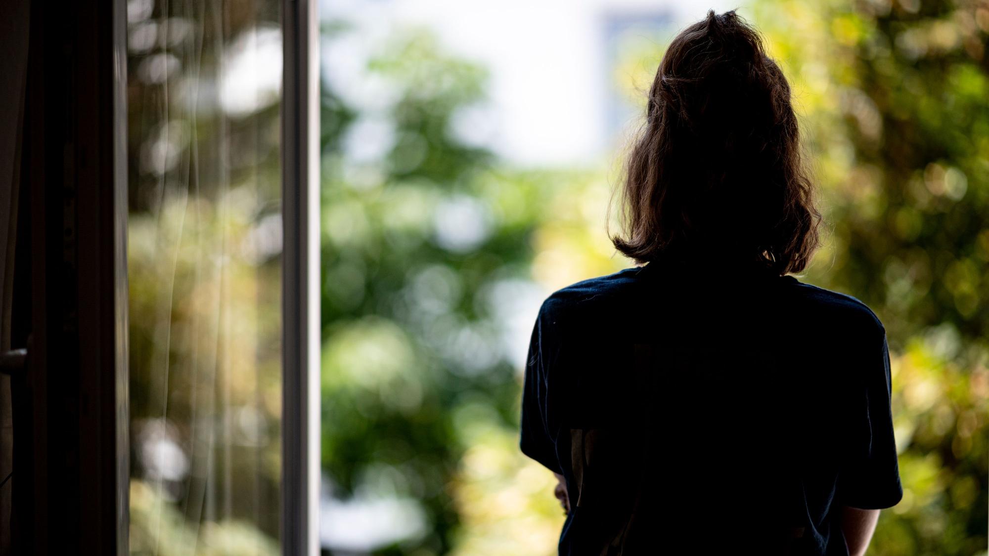 Eine Frau steht in ihrer Wohnung an einem Fenster.