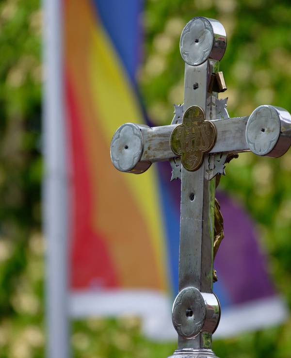 Ein Kreuz vor einer Regenbogenfahne.