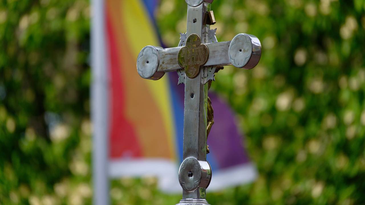 Ein Kreuz vor einer Regenbogenfahne.