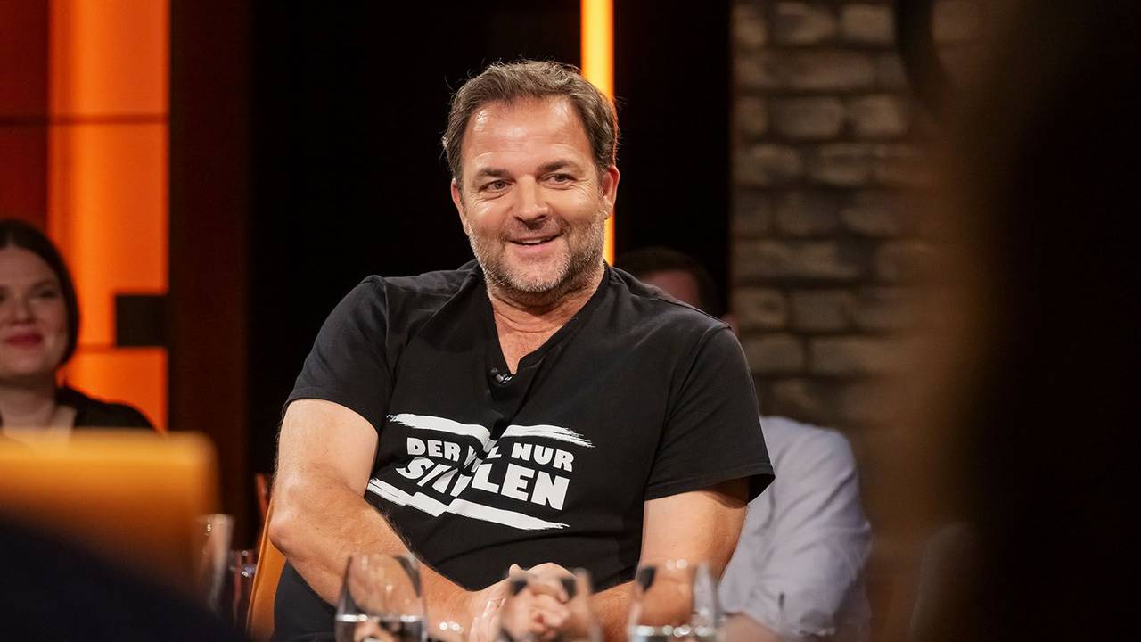 Martin Rütter sitzt auf einem Stuhl. Vor ihm stehen mehrere Gläser auf einem Tisch.