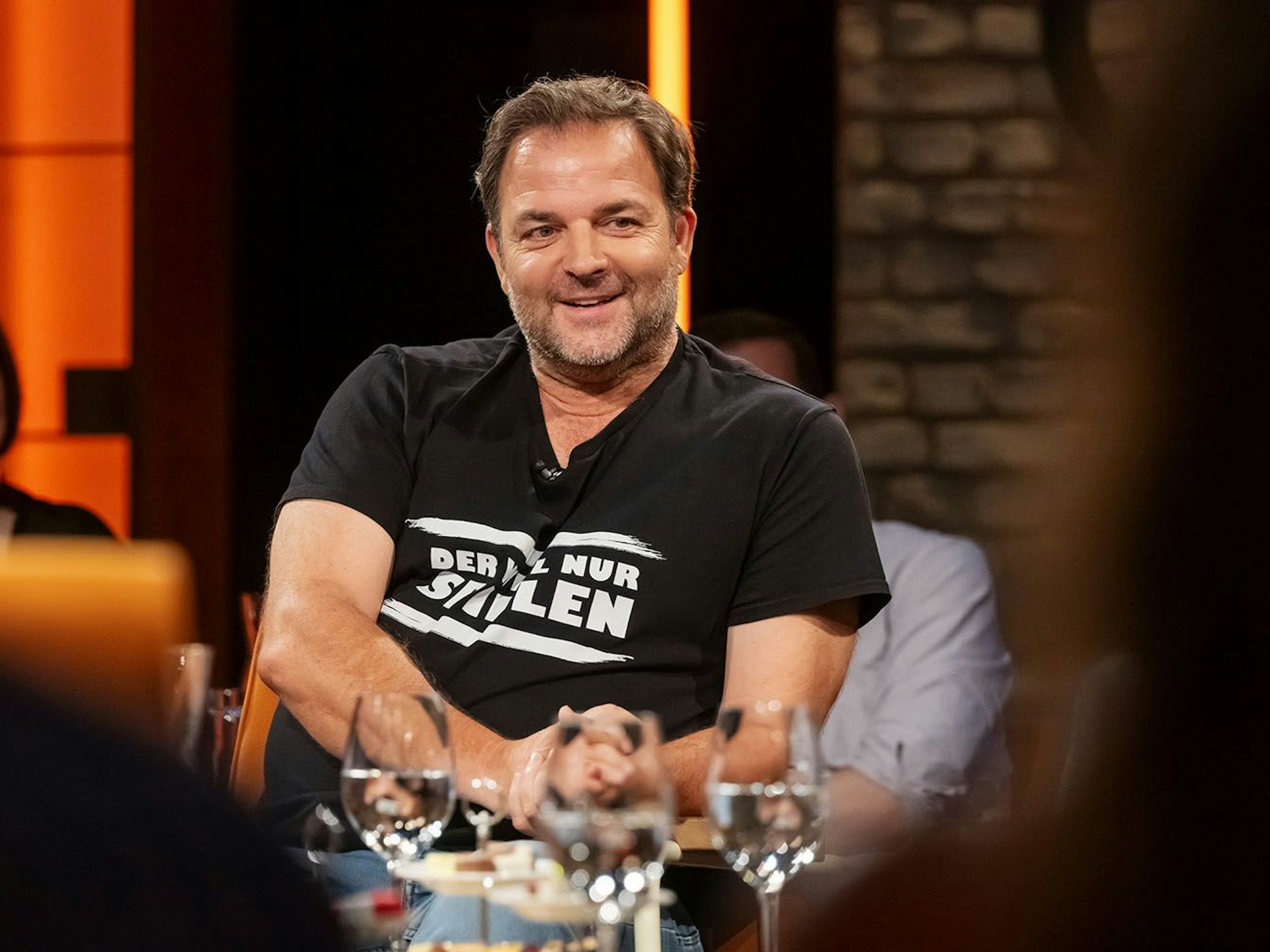 Martin Rütter sitzt auf einem Stuhl. Vor ihm stehen mehrere Gläser auf einem Tisch.