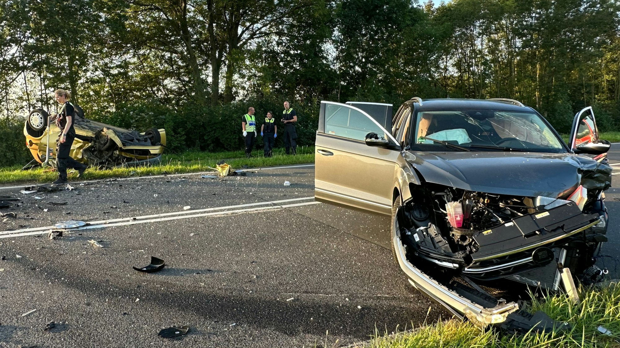 Ein beschädigtes Auto steht auf der Fahrbahn, die von Trümmerteilen übersät ist. Neben der anderen Fahrbahn liegt ein Auto auf dem Dach.
