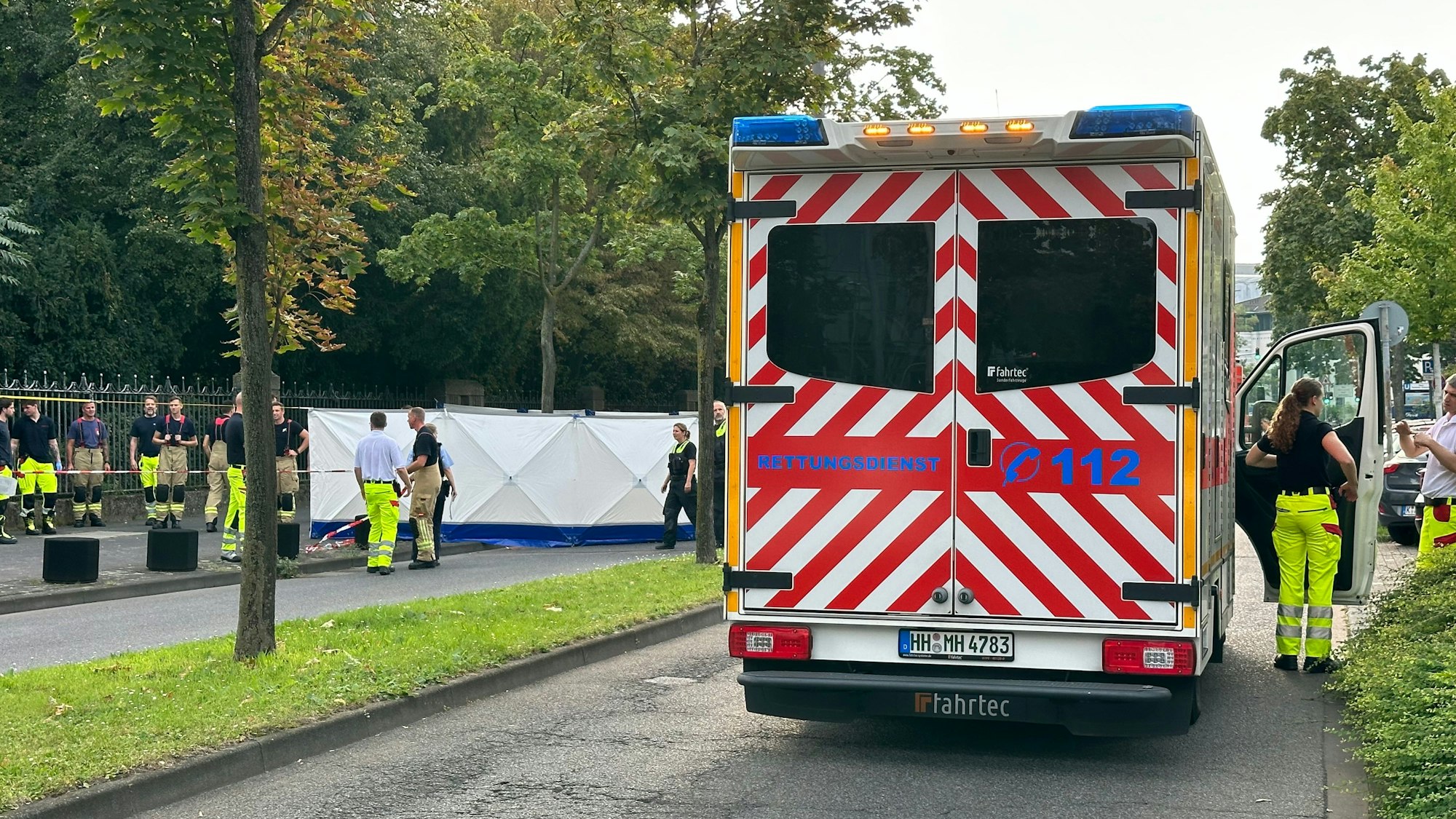 Über die Straße ist ein Blickschutz gespannt, rechts steht ein Rettungswagen.