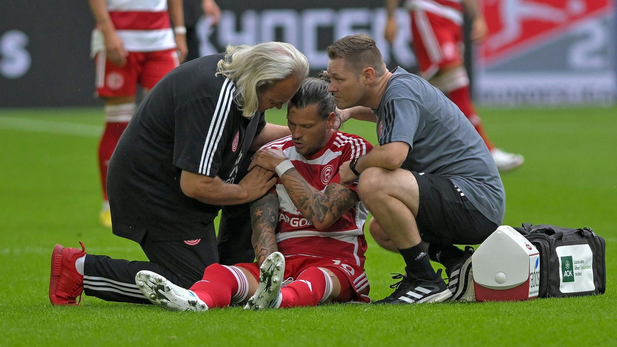 Daniel Ginczek sitzt auf dem Rasen und wird von Dr. Ulf Blecker behandelt.