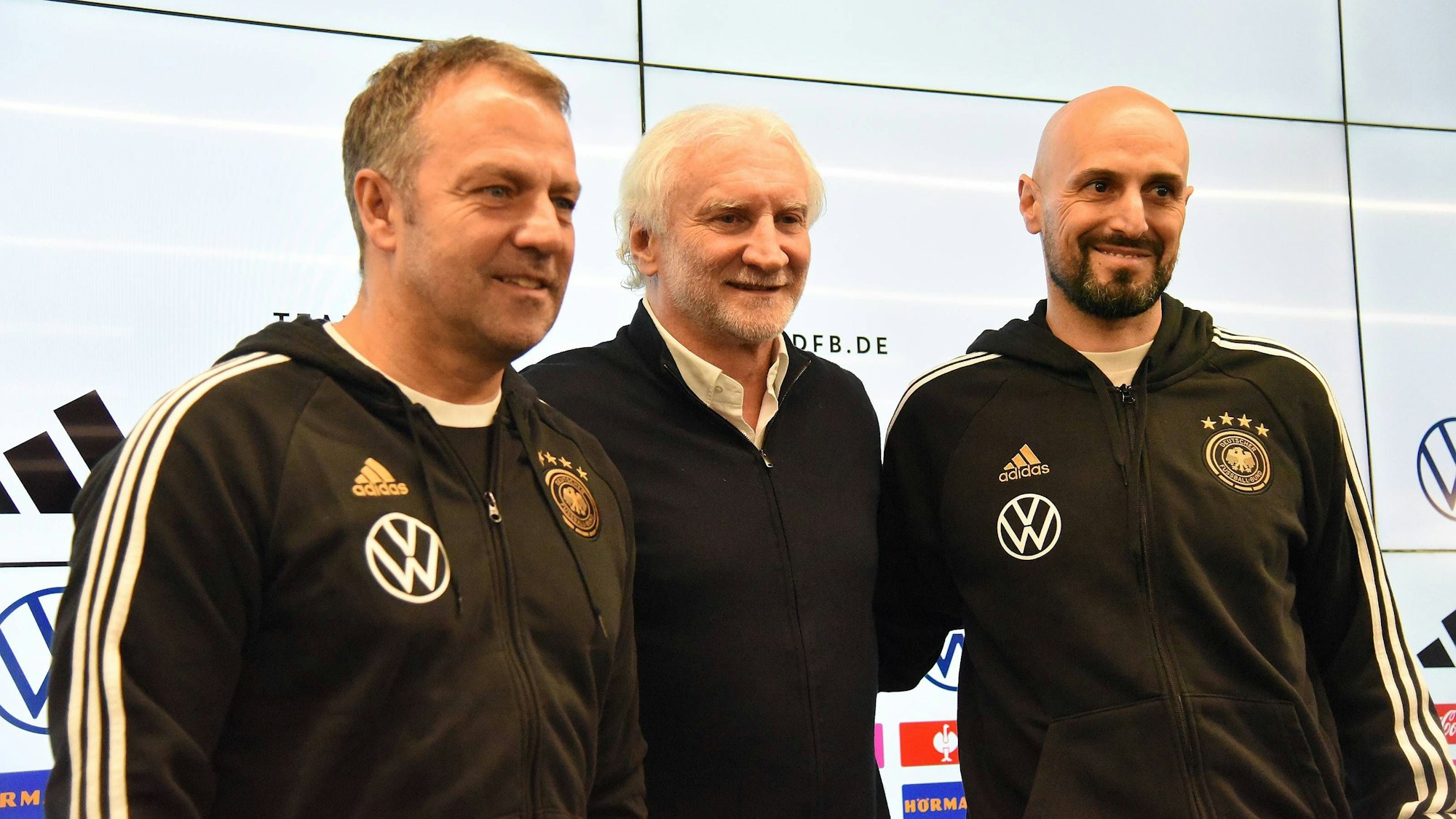Hansi Flick, Rudi Völler und Antonio Di Salvo stehen bei einer Pressekonferenz nebeneinander.