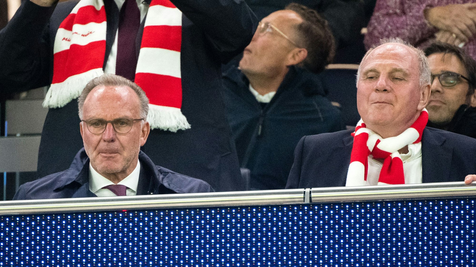 Karl-Heinz Rummenigge und Uli Hoeneß sitzen nebeneinander auf der Tribüne, Hoeneß trägt einen rot-weißen Fanschal.