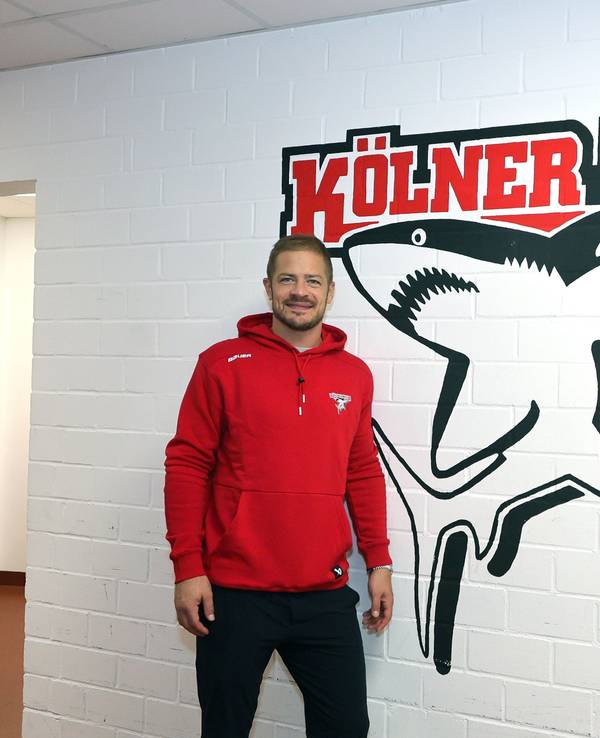 Moritz Müller (Haie) steht vor dem Logo des KEC in der Arena-Kabine.