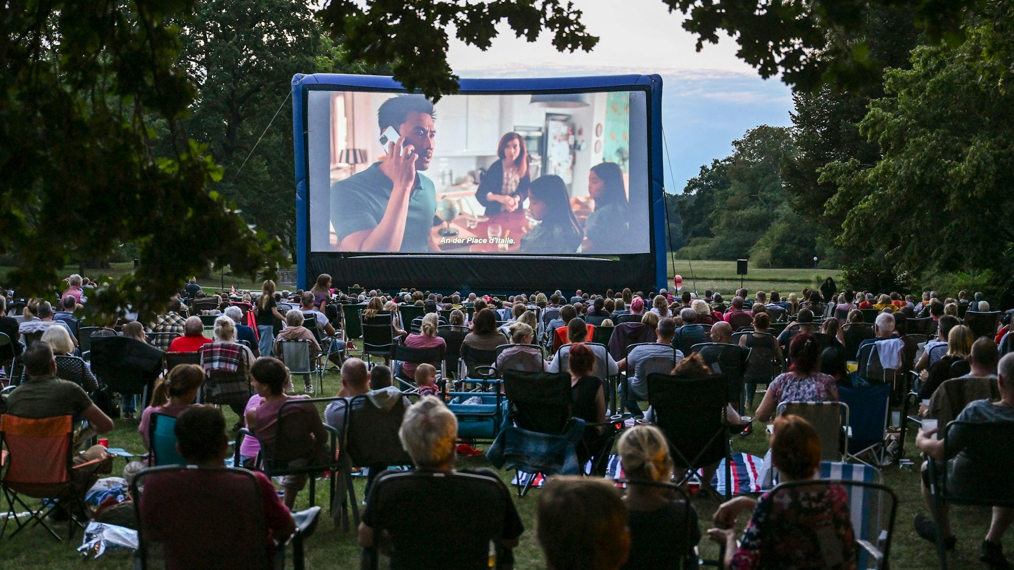 Zahlreiche Zuschauer verfolgen im Freiluftkino im Schlosspark Oranienburg am Abend in der Dämmerung einen Film.