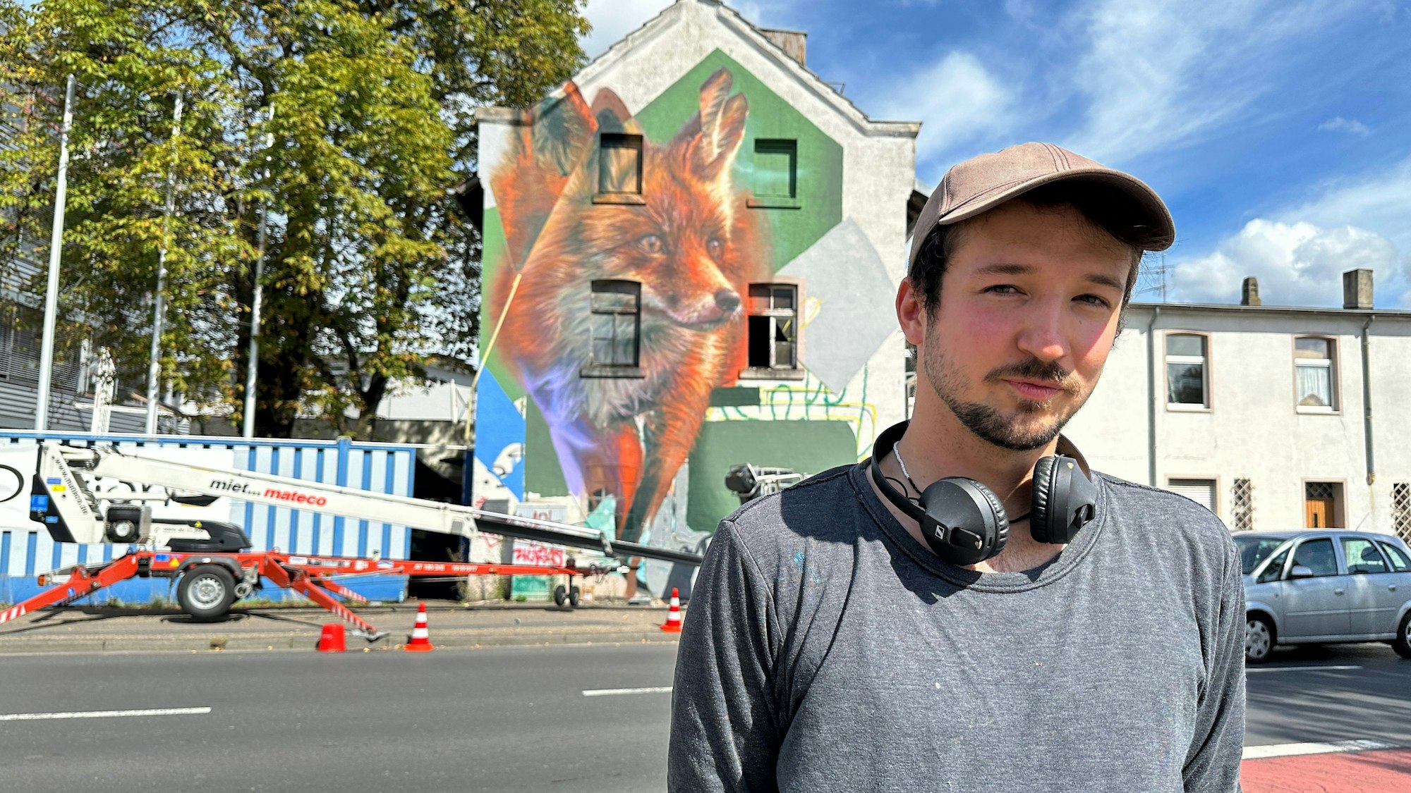 Straßenkünstler Roman De Laporte – im Hintergrund das Fuchsgemälde auf einer Hauswand.