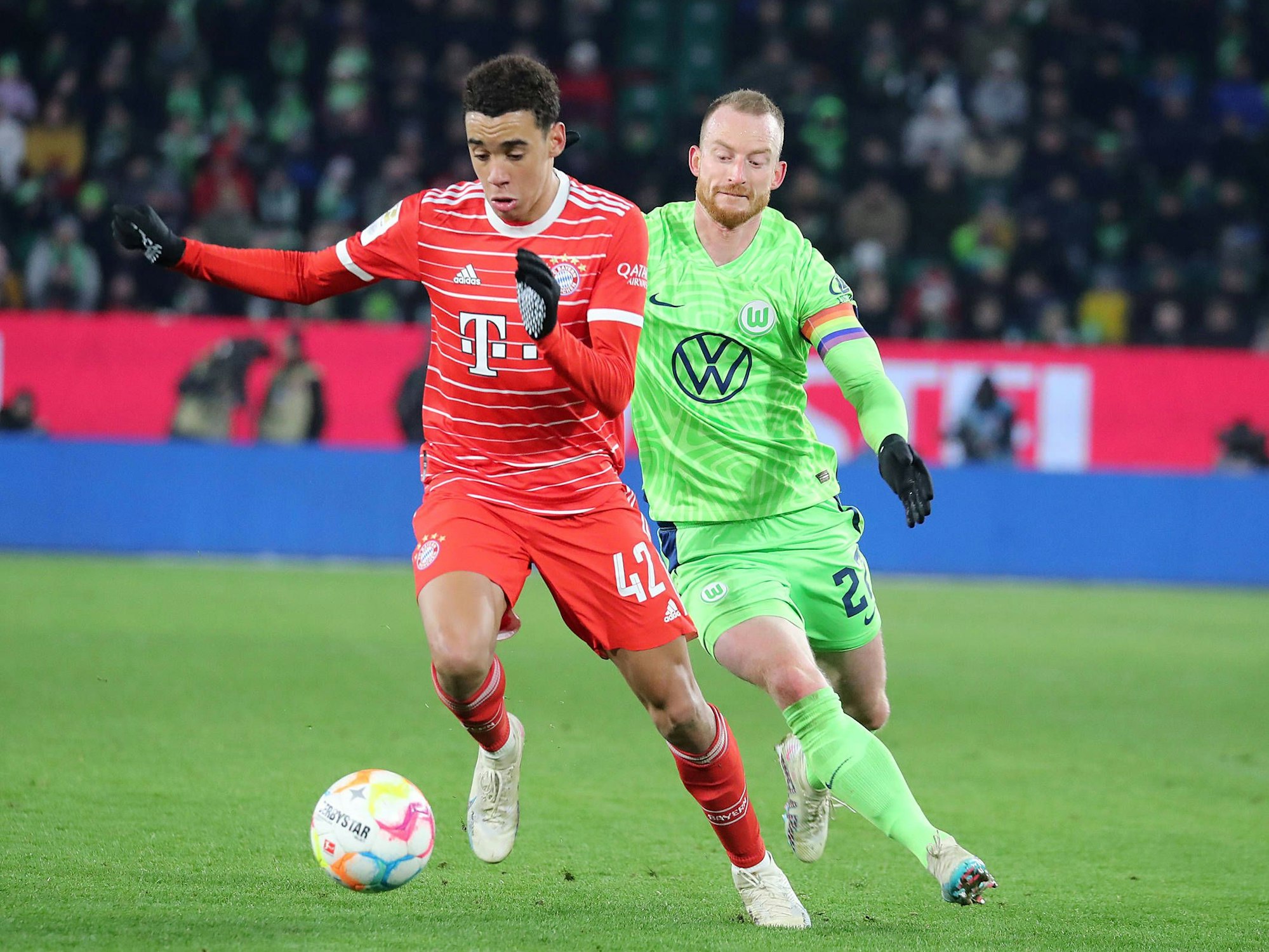 Jamal Musiala vom FC Bayern München führt den Ball, Maximilian Arnold vom VfL Wolfsburg rennt hinterher.