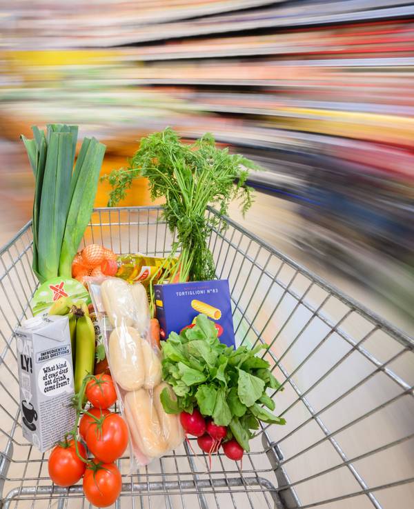 Ein mit Lebensmittel gefüllter Einkaufswagen wird durch einen Supermarkt geschoben.