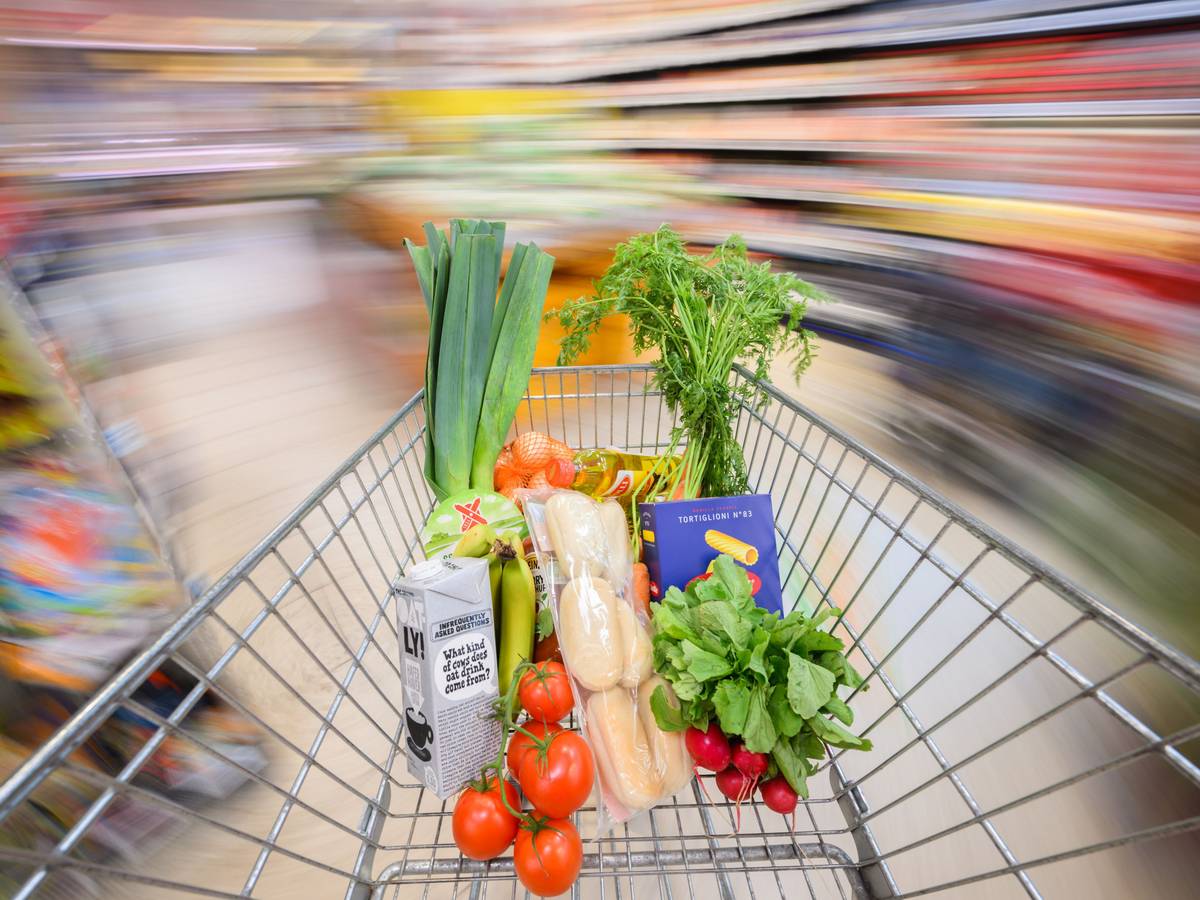 Ein mit Lebensmittel gefüllter Einkaufswagen wird durch einen Supermarkt geschoben.