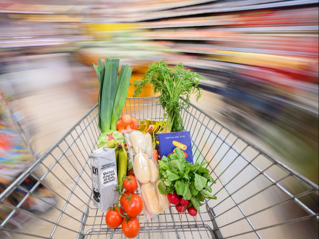 Ein mit Lebensmittel gefüllter Einkaufswagen wird durch einen Supermarkt geschoben.