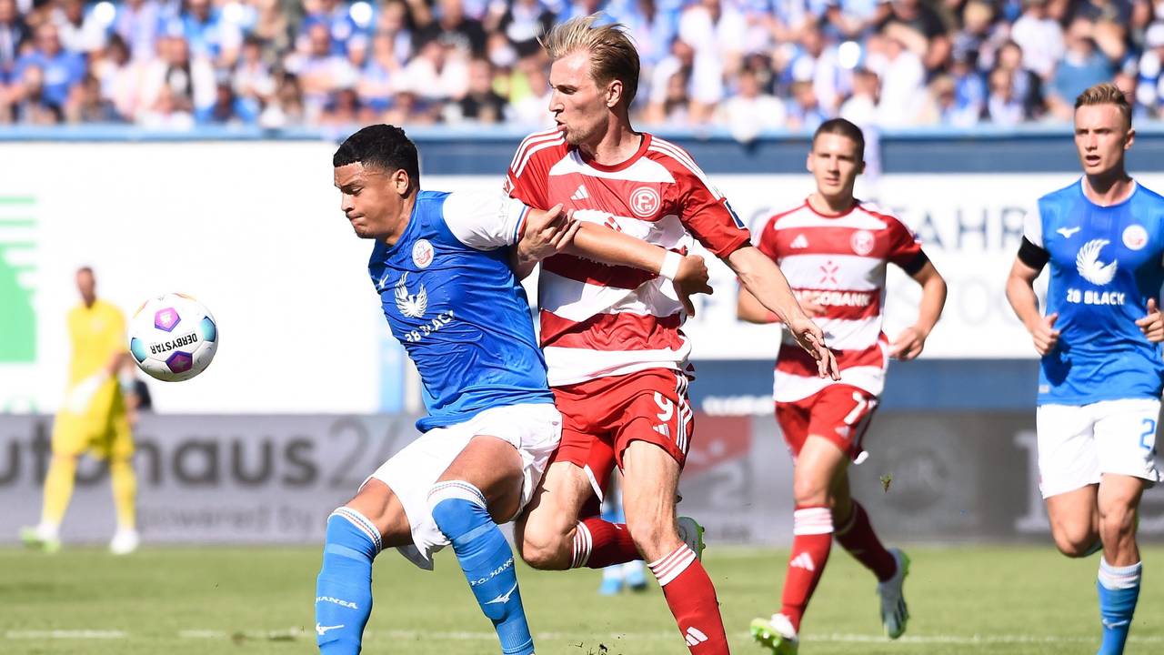 Rostocks Jonas David (l) behauptet den Ball gegen Düsseldorfs Vincent Vermeij im Mittelfeld.