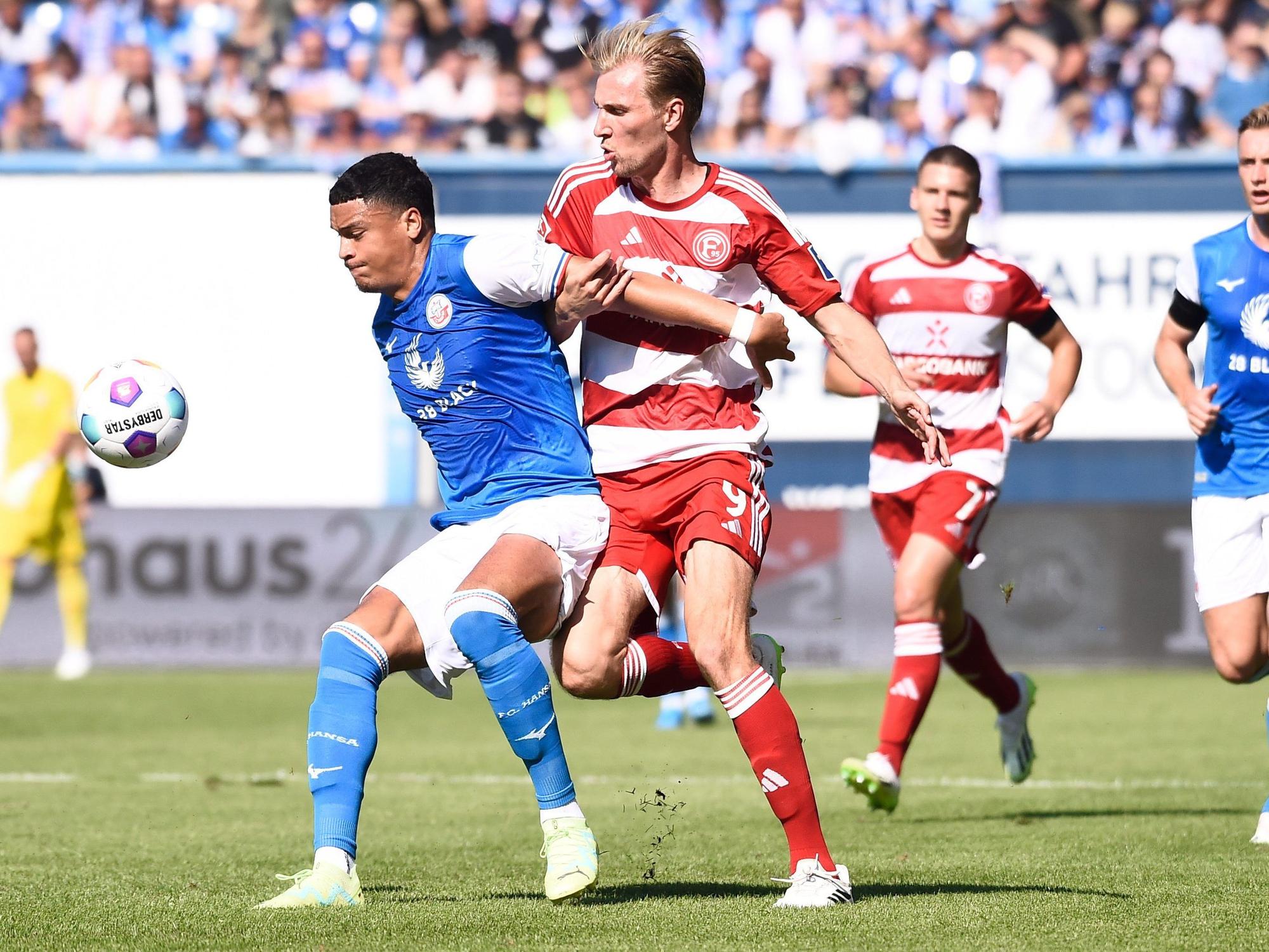 Rostocks Jonas David (l) behauptet den Ball gegen Düsseldorfs Vincent Vermeij im Mittelfeld.